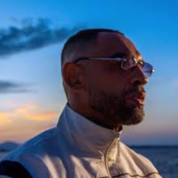 Profil d'un homme portant des lunettes et une veste dans un paysage au coucher du soleil.